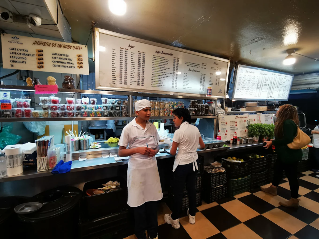 Meseros parados frente a la barra de la lonchería Ojo de Agua en CDMX.
