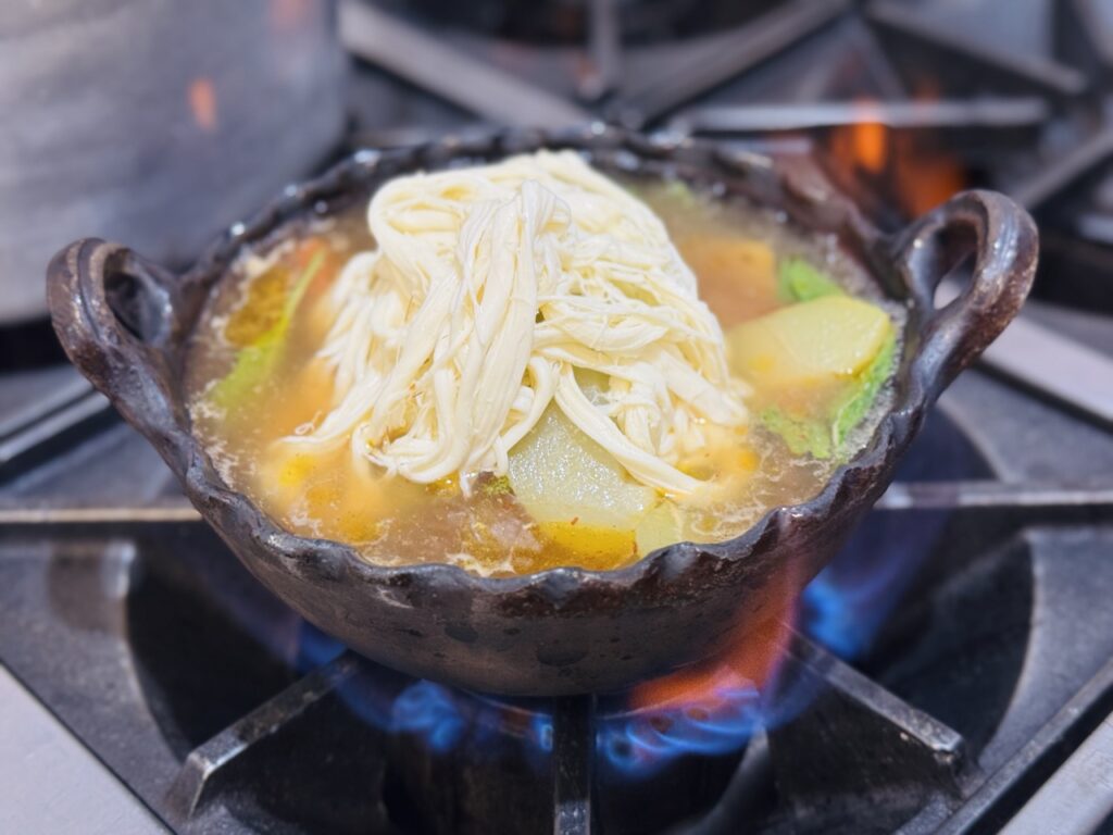 Caldo tlalpeño servido en un plato de barro calentándose directo al fogón.