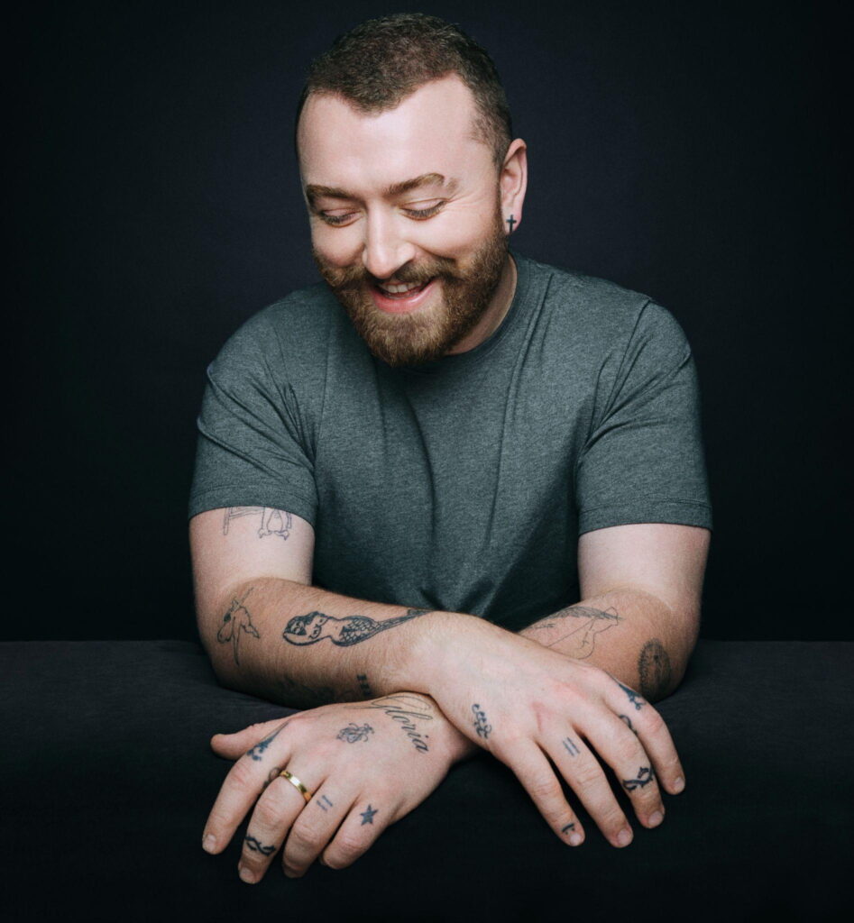 Retrato del cantante Sam Smith usando una playera gris y soriendo.