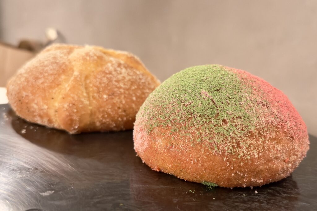 Un pan de muerto tradicional y otro con azúcar verde y rosa.
