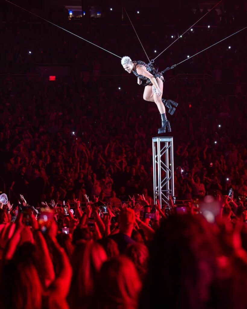 PINK en su Carnival Tour usando arneses y parada en una torre de metal.