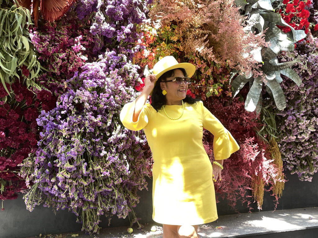 Mujer vestida de amarillo posando para una foto con un fondo de flores.