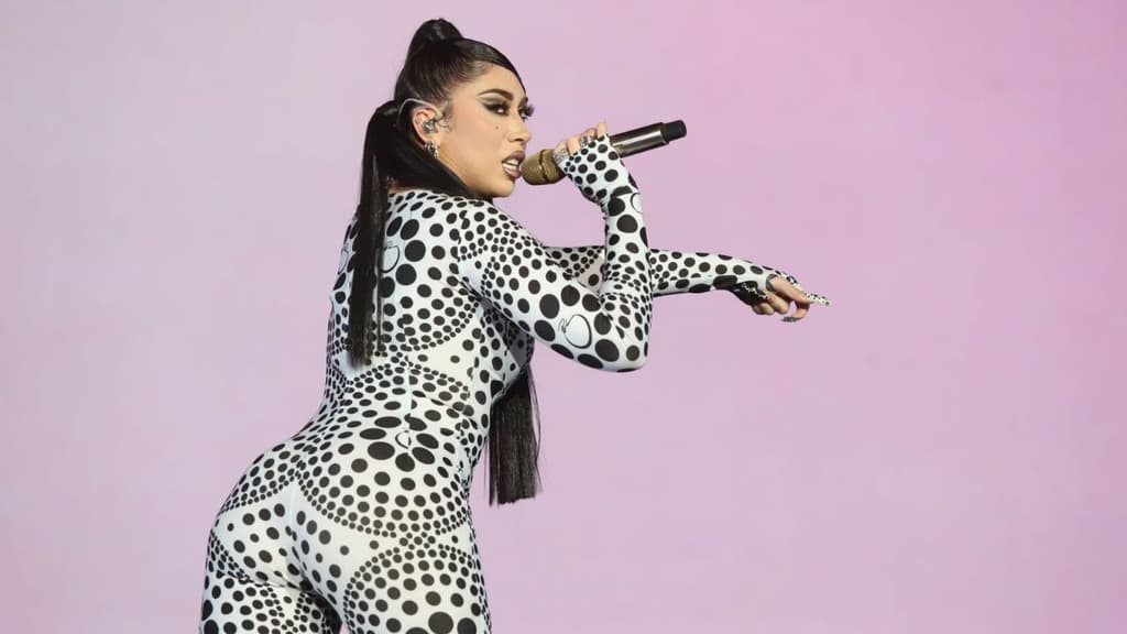 Kali Uchis cantando en el escenario, usando un body blanco con negro.
