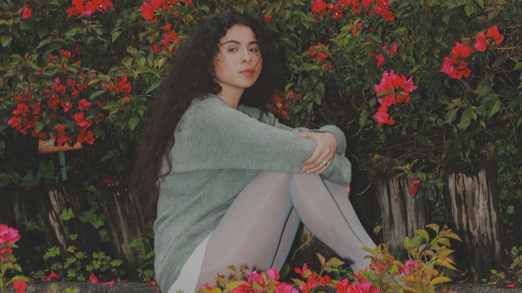 Retrato de Silvana Estrada sentada en un jardín rodeada de flores.