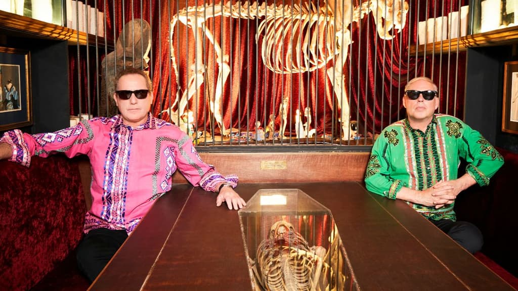 Retrato del dúo OMD usando camisas de colores rosa y verde.