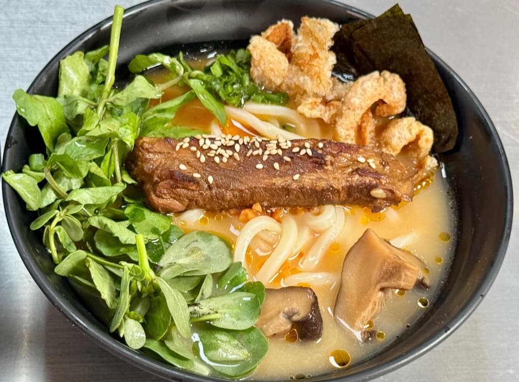 Plato con fideo udon, chicharrón, berros y pork belly.